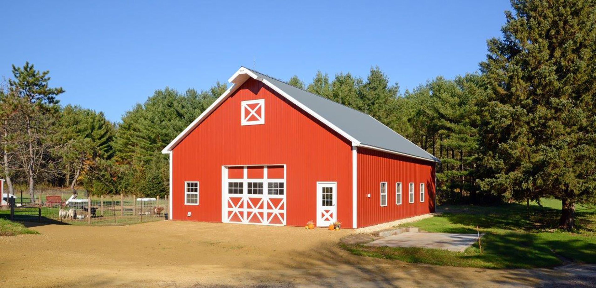 Red agricultural post frame goat barn with white trim