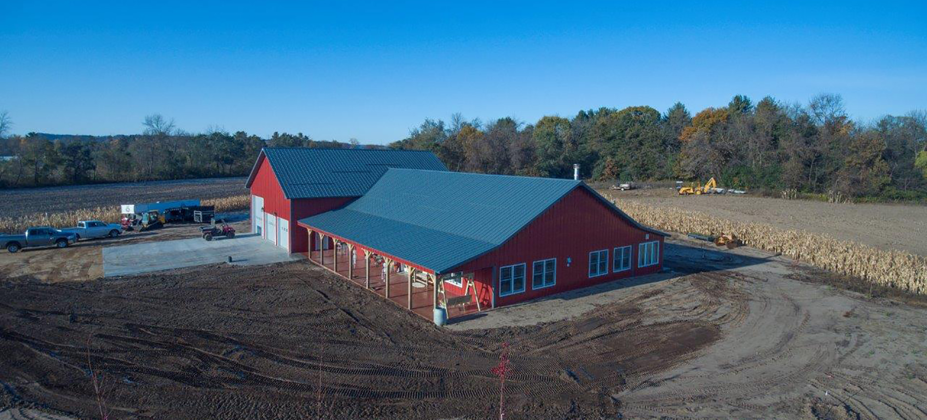 Large red suburban postframe building with three garage doors and a lengthy front awning / porch